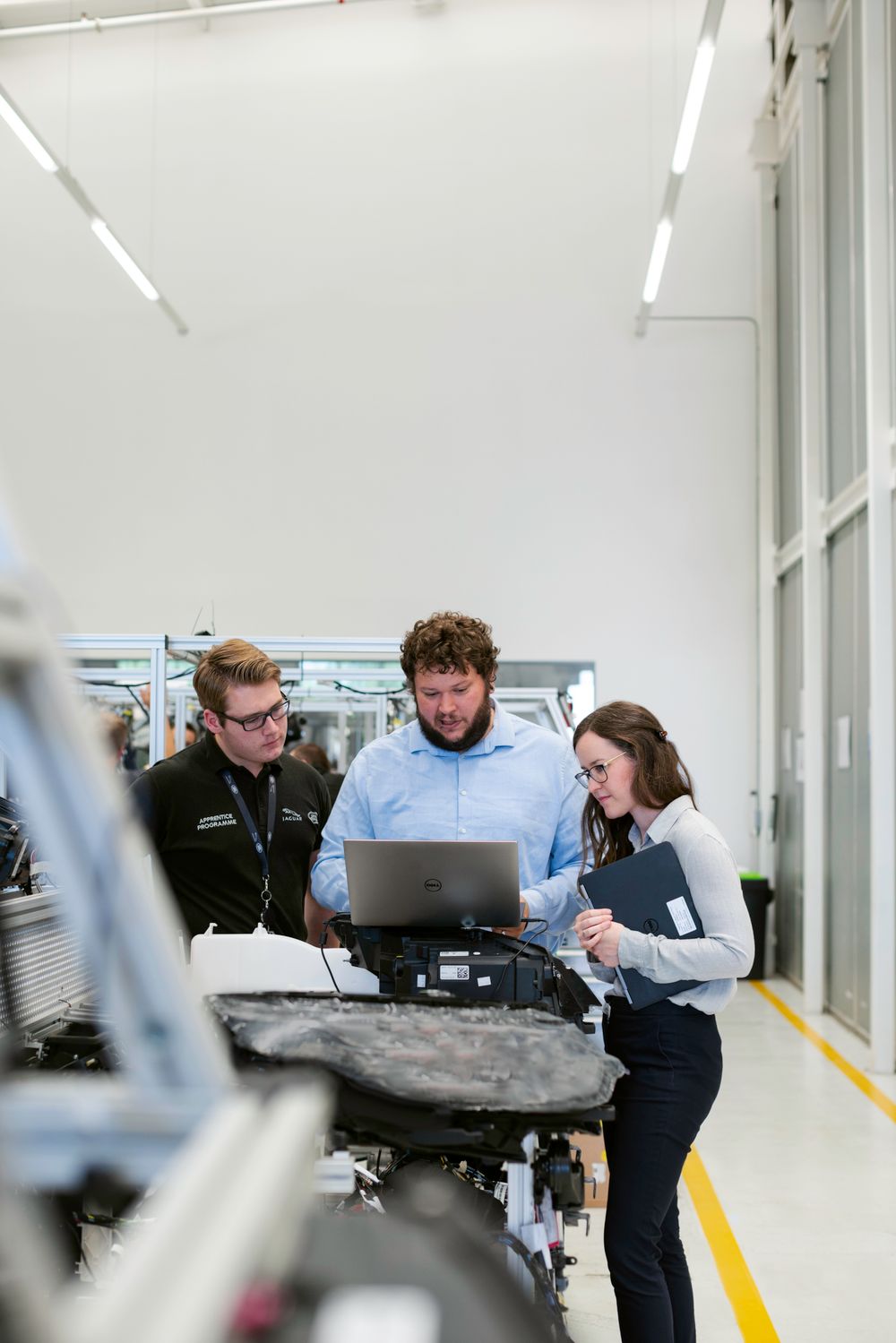 Three engineers reviewing a laptop together beside workshop equipment